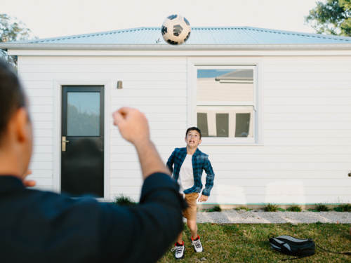 Father and son playing with a soccer ball outside the house. - Australian Stock Image