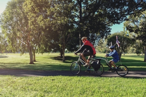 Father and son riding tag along bike through the park