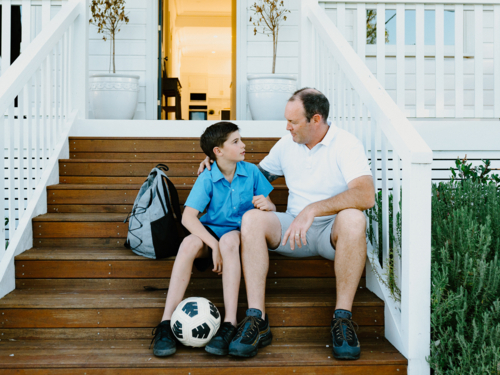 Father and son sitting on the wooden steps of their porch. - Australian Stock Image