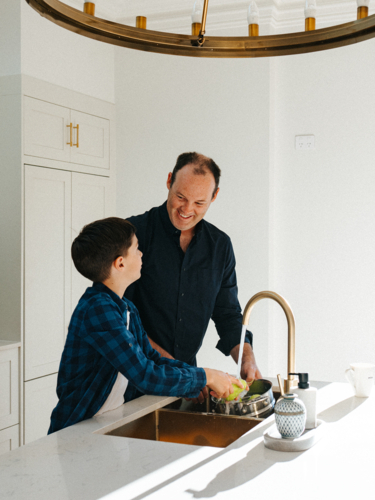 Father and son washing apples in the kitchen sink. - Australian Stock Image