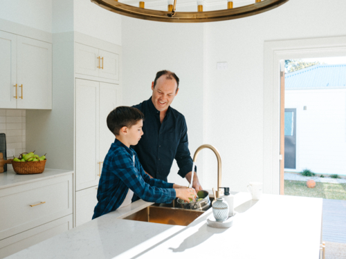 Father and son washing apples in the kitchen sink. - Australian Stock Image