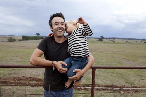 Father and young son laughing together on old gate on rural farm - Australian Stock Image