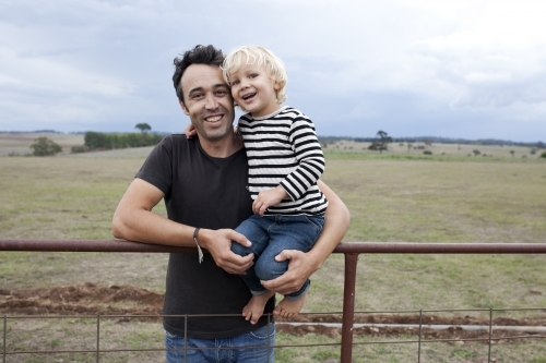 Father holding happy young son on an old farm fence - Australian Stock Image