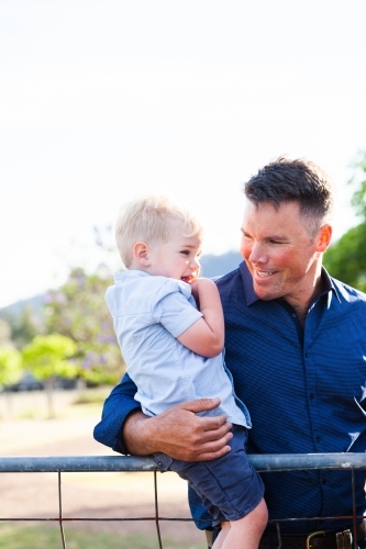 Father holding son on farm gate - Australian Stock Image