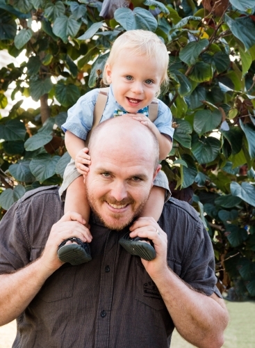 Father holding son on shoulders while smiling at the camera. - Australian Stock Image