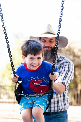 Father pushing son on the swing at the park - Australian Stock Image
