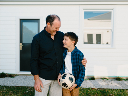 Father standing beside his son holding a soccer ball. - Australian Stock Image