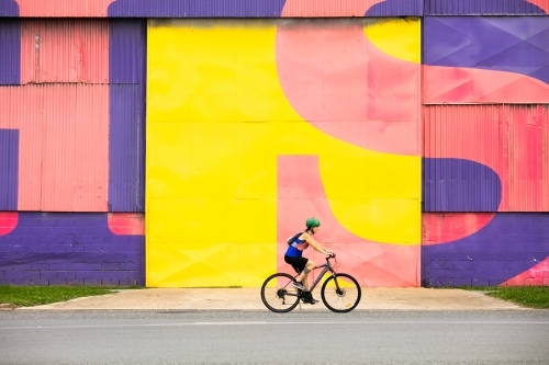 Female Cyclist Riding by a Colourful Wall - Australian Stock Image