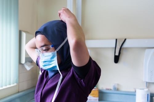 Female dentist wearing hajib putting on surgical mask - Australian Stock Image