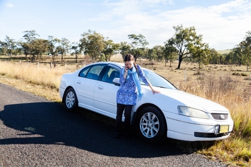 Female driver on phone beside car stopped on roadside in rural area - Australian Stock Image