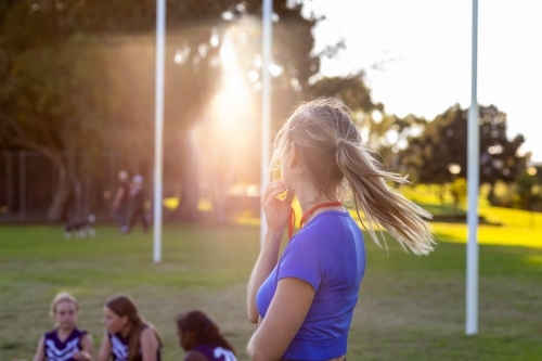 female football coach turning away with girls sitting behind on football field - Australian Stock Image