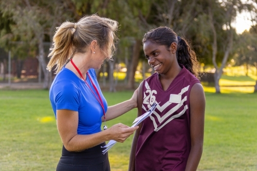 female footy coach speaking with encouragement to shy aboriginal girl - Australian Stock Image