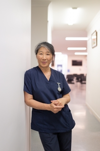 Female healthcare worker leaning on the wall smiling - Australian Stock Image