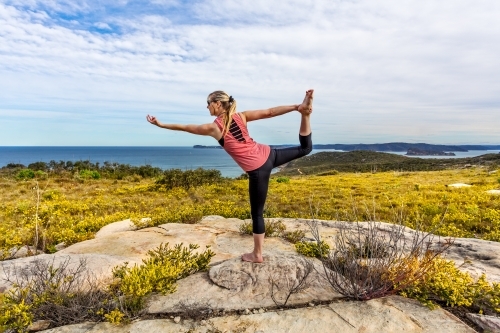 Female in outdoor coastal setting with wildflowers blooming doing yoga