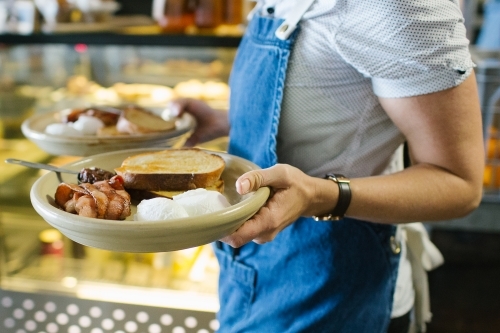 Female server serving two breakfast plates with toast, eggs, and bacon - Australian Stock Image