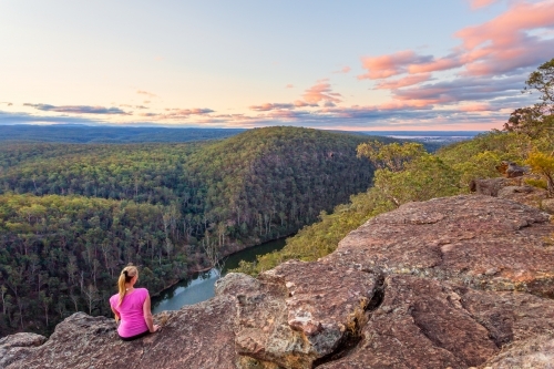 Female sitting on a rocky cliff with views over the Nepean Gorge and Blue Mountains, Australia