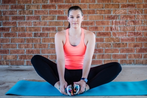 Female stretching on yoga mat with brick wall background - Australian Stock Image