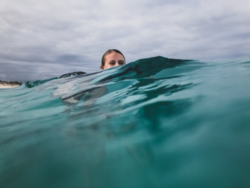 Female teenager with head semi submerged floating in ocean on glassy overcast day - Australian Stock Image