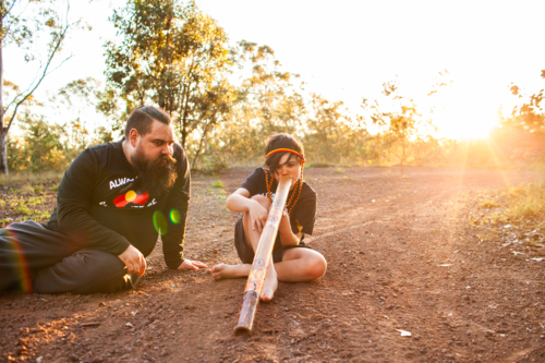 First Nations Australian father teaching Aboriginal son to play didgeridoo in rural Australia - Australian Stock Image