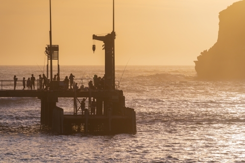 Fishermen and sightseers on a jetty in front of a golden sky - Australian Stock Image