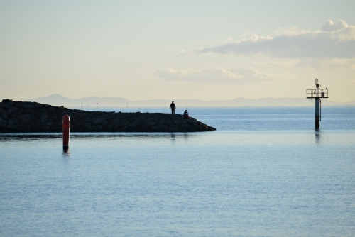 Fishermen fishing off the rocks at the end of a pier in the bay - Australian Stock Image