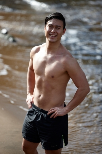 Fit Asian man smiling at beach wearing only shorts - Australian Stock Image