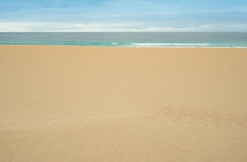 Flat, untouched sand leading to calm ocean in the background - Australian Stock Image