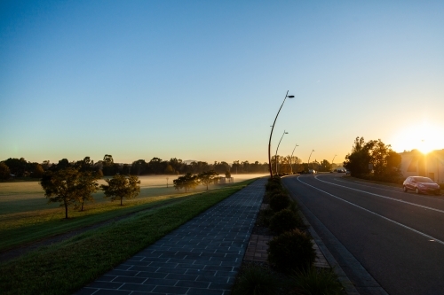 footpath on levee bank with mist covered playing field and road in morning light - Ryan Ave - Australian Stock Image
