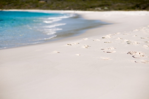 Footprints on white sand beach with turquoise water - Australian Stock Image