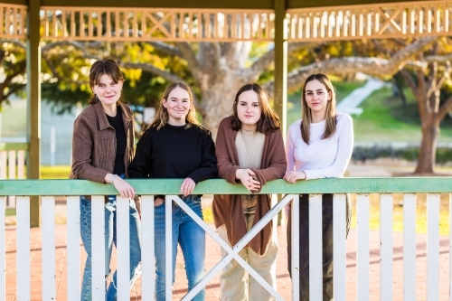 Four friends leaning on railing of gazebo in park smiling - Australian Stock Image