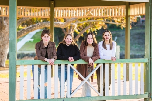 Four girls leaning on railing at park smiling - Australian Stock Image