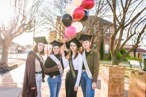 Four high school graduates holding balloons standing in town centre
