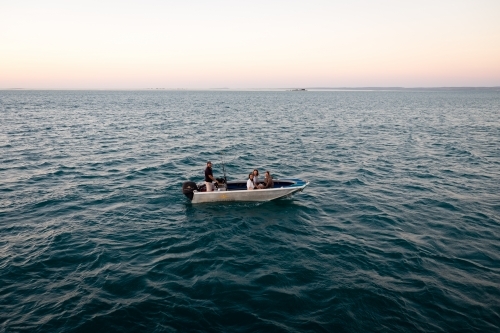 Four people sitting in a dinghy in remote ocean at sunset - Australian Stock Image