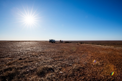 four wheel drive and people in brown landscape with blue sky and blazing sun - Australian Stock Image