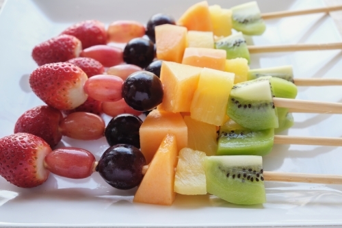 Fresh rainbow fruit skewers on white plate - Australian Stock Image
