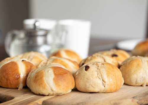 freshly made hot cross buns on table with teapot and cups - Australian Stock Image