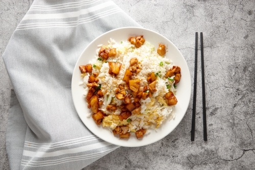 Fried rice topped with pineapple chicken served in a white plate. - Australian Stock Image