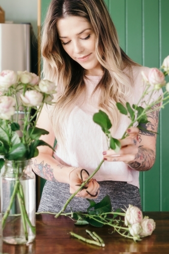 Girl at home trimming fresh pink roses and arranging in a vase - Australian Stock Image