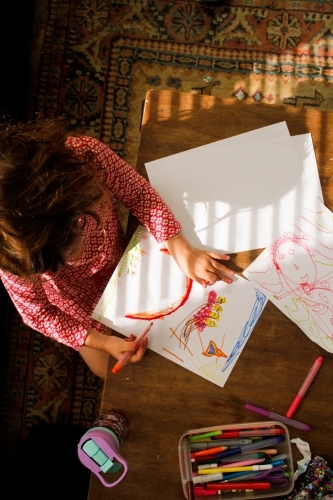 Girl drawing a rainbow doing art on paper with texta - Australian Stock Image