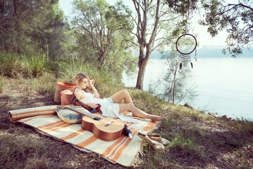 Girl having a picnic by the river with a guitar - Australian Stock Image