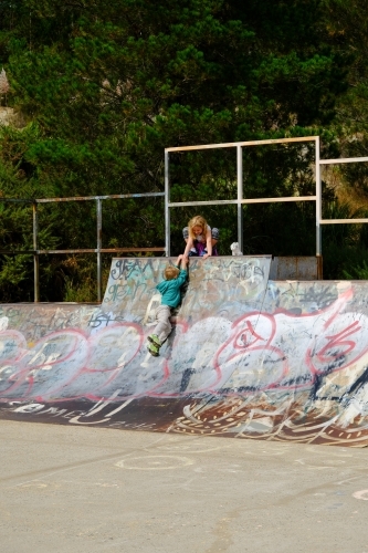Girl helping boy up a skate park ramp - Australian Stock Image