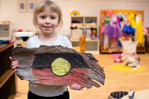Girl holding painted Aboriginal flag on tree bark