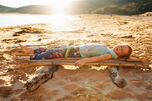 Girl laying on a bamboo raft on the beach - Australian Stock Image