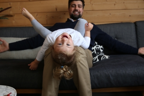 Girl lying on dad's lap on lounge looking at camera - Australian Stock Image