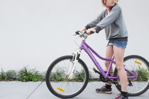 Girl pausing as she rides her bike along a suburban street - Australian Stock Image