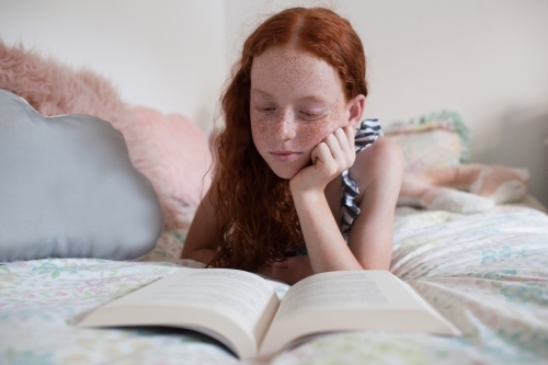 Girl reading a book on a bed - Australian Stock Image