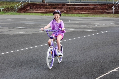 Girl riding bicycle wearing helmet at sporting complex - Australian Stock Image