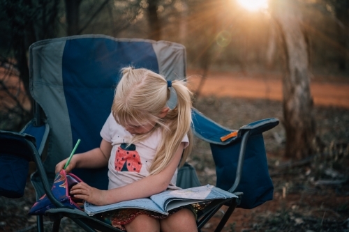 girl sitting in a camp chair at sunset drawing - Australian Stock Image