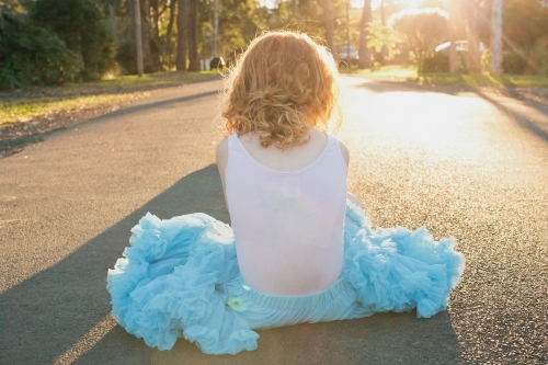 Girl sitting on a road in a blue tutu skirt - Australian Stock Image