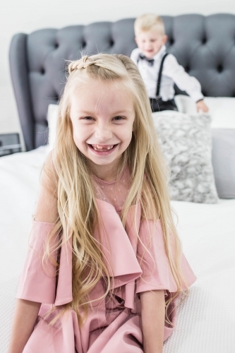 Girl sitting on end of bed with boy standing behind - Australian Stock Image
